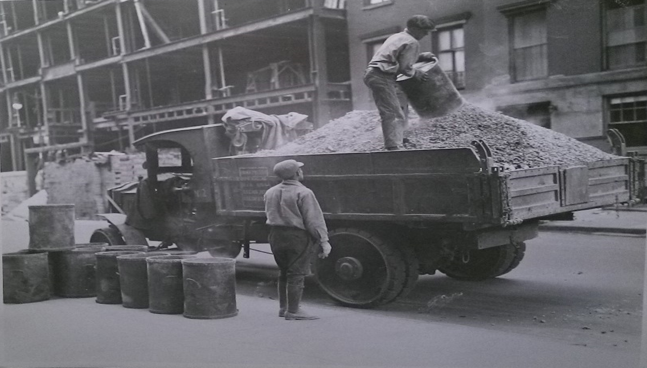 Two men hauling garbage into an open refuse truck.